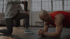 Fitness trainer tapping smartwatch guiding client holding plank while grid building metrics chart. Strength, progress, coaching, biometric, training, innovation, health - Powered by Shutterstock - Get 15% off with code: PIKWIZARD15