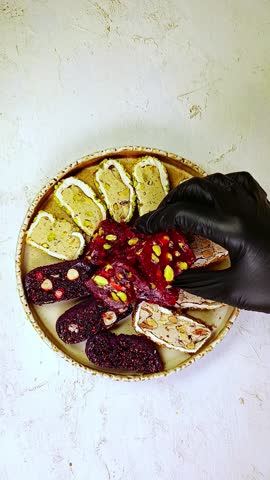 Sliced ​​Turkish delight assortment with cream filling, pistachio, almond, hazelnut, figs and cranberry on the plate. Putting the sweets on the plate. Local name: fistikli fitil lokum