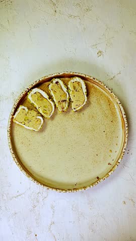 Sliced Turkish delight assortment with cream filling, pistachio, almond, hazelnut, figs and cranberry on the plate. Putting the sweets on the plate. Local name: fistikli fitil lokum