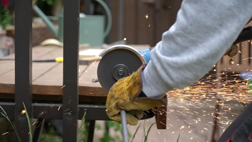 Man cutting metal rod with angle grinder, sparks flying. Close-up of construction work using power tools outdoors.