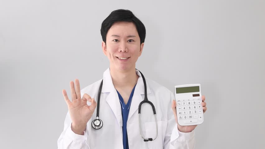 A smiling Asian male doctor in a white coat holding a calculator