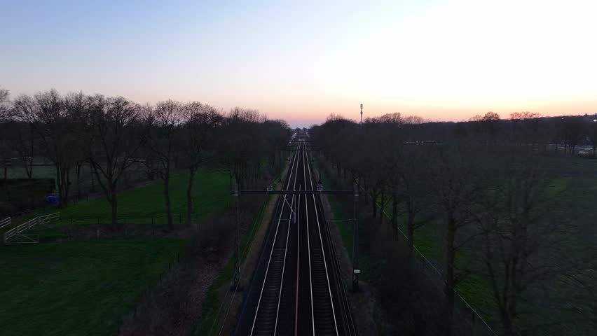 Overview drone view of the railroad tracks stretching into the horizon in rural dusk scenery.