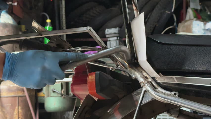Close-up of blue-gloved hand welding a metal bar with bright sparks and protective gear.