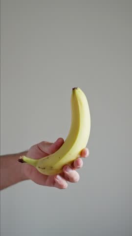 Banana Fruit Spinning and Rotating Isolated on White Background Suspended in the Air and Caught by a Male Hand on White Background, Isolated Slow Motion. Vertical video.