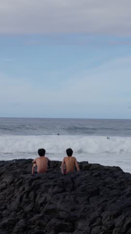 Two children are happily enjoying the breathtaking ocean view, captivated by surfers skillfully riding the waves. Slow motion
