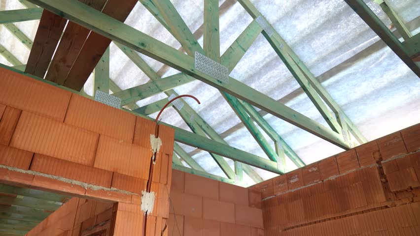 Exposed timber roof trusses above unfinished brick walls inside house under construction
