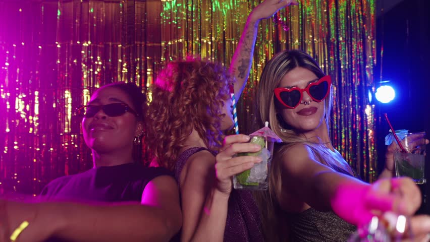 Cheerful women dancing and drinking cocktails in photo booth