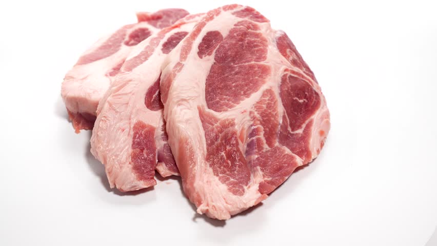Raw meat on white. Several slices of raw pork lie on a white background and rotate. The detailed structure of the meat is in the foreground.