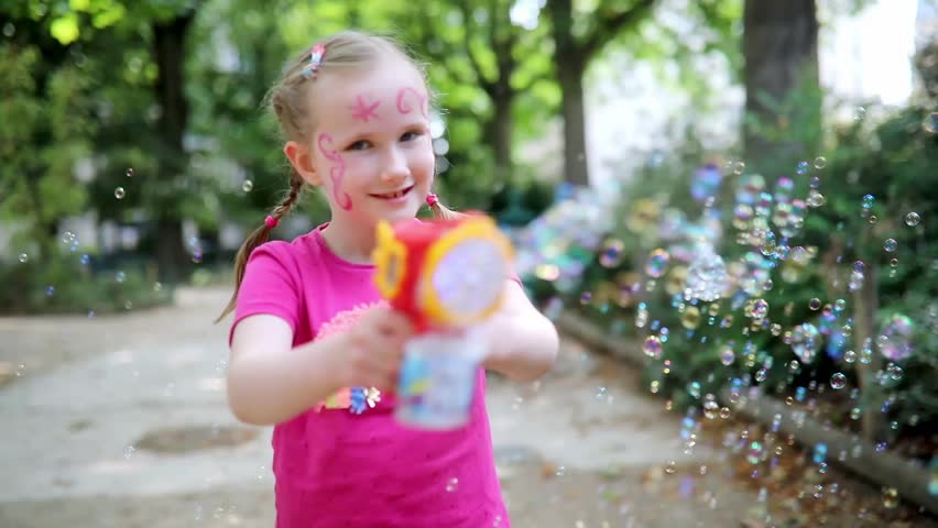 Adorable happy little girl blowing soap bubbles in the park