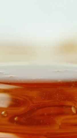 Golden honey dripping from creating elegant streams that flow gracefully downward. The viscous honey forms continuous golden ribbons. A jar filled with honey. Close-up. Macro photography natural food.
