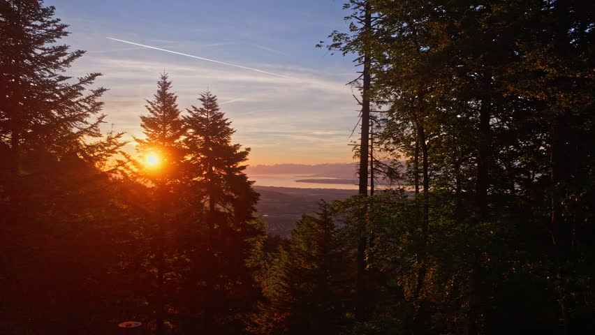 Aerial sunrise over Lake Geneva with fiery orange and red skies, panoramic Alpine views, and tranquil morning reflections on Lac Léman from the Jura.