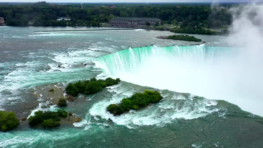 High drone orbit establishing of Niagara Falls showing massive curved drop and white mist rising upward
