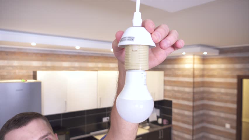 Close up of man changing light bulb at ceiling lamp at home. Turning it on. Bulb shining in kitchen. Do it by himself at home.
