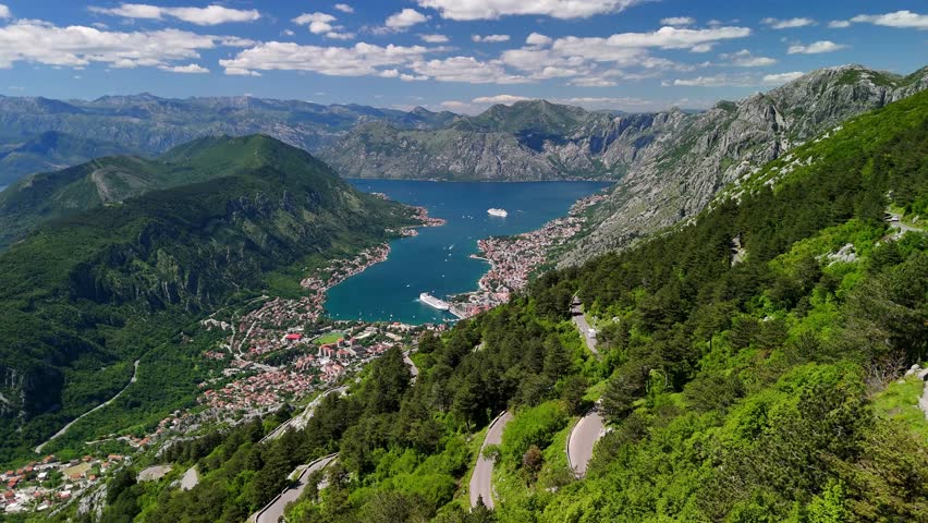 Aerial drone view of Kotor Bay Boka and mountains from a mountain viewpoint in Montenegro. Tourist boats are visible on the horizon.
