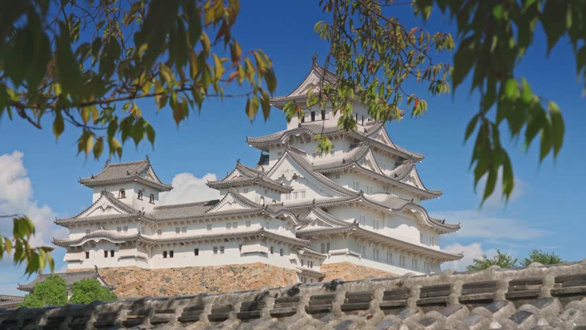 Himeji, Japan - Sep 24 2024, 4k, panoramic view of Himeji Castle, White Heron Castle from below, through tree foliage in daytime with blue sky and clouds, without people, Himeji, Japan