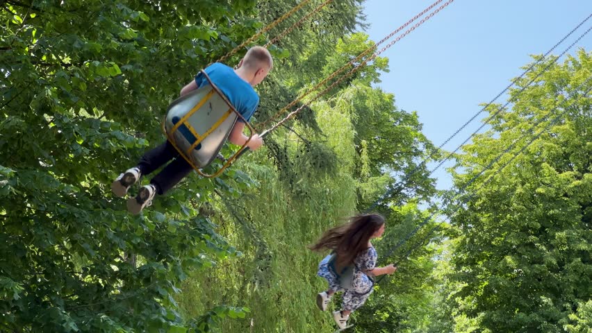 Summer adventure at the fair: Youngsters on a classic chain carousel, feeling the joy of flying.Low angle view of children having fun on a spinning wave swinger, soaring through the air in a park