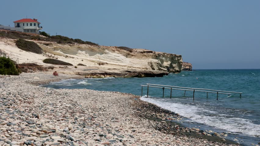 Rocky Beach with White Cliffs and Blue Sea in Cyprus, Scenic rocky beach with smooth pebbles, striking white cliffs, and turquoise waves along the Mediterranean.