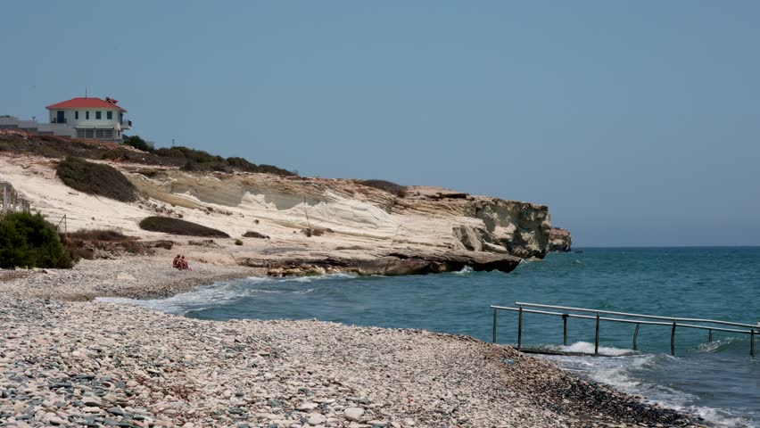 Rocky Beach with White Cliffs and Blue Sea in Cyprus, Scenic rocky beach with smooth pebbles, striking white cliffs, and turquoise waves along the Mediterranean.