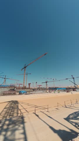 Large construction site with several busy cranes. Working progress at construction site. Builders and lifting machineries working at huge industrial construction site. Vertical timelapse footage