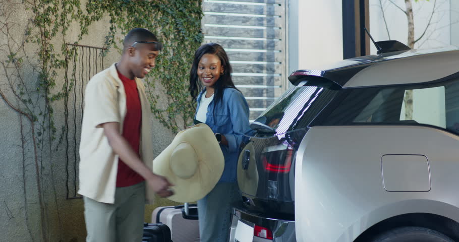 African American couple arriving at carport loading luggage and sunhat into SUV checking smartphone. Adventure, travel, outdoor, lifestyle, modern, transportation, leisure