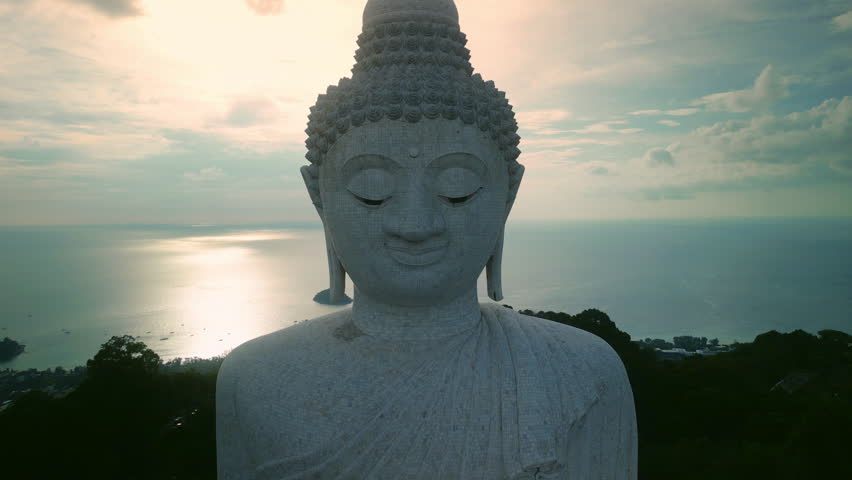Kind face of Phuket Big Buddha statue against calm sunset ocean aerial view. Amazing Asian culture memorial presenting Buddhism religion on mountain. Mindfulness concept