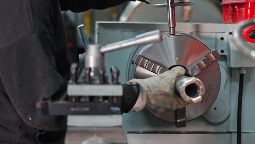 Worker installs metal part into lathe chuck, manual setup in machine shop, Precision alignment ensures secure clamping for accurate turning operations