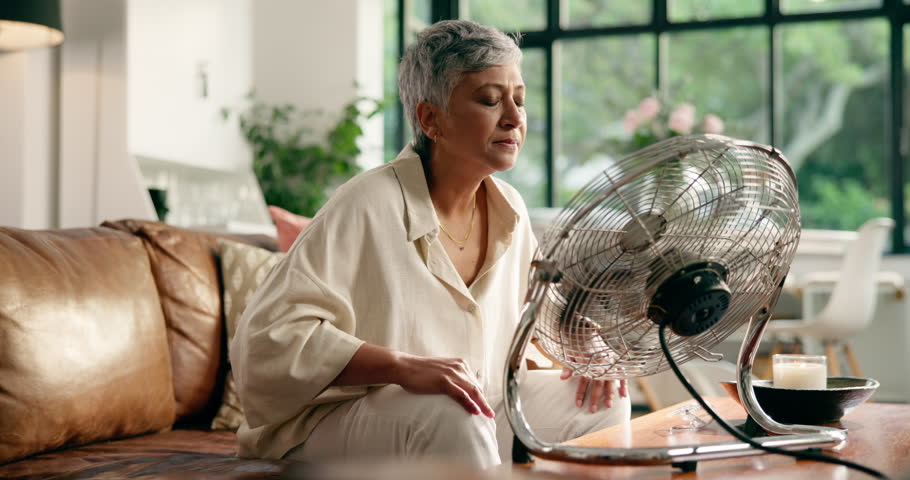 Senior woman, menopause and breathing with fan for hot flashes in relax for treatment at home. Mature, female person or smell with blowing air for relaxation technique, candle incense or calm remedy