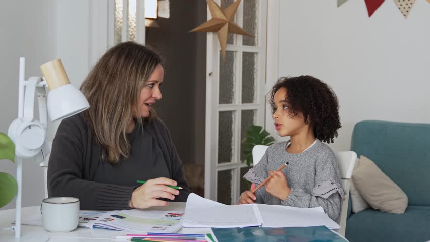 Caucasian mother and African American daughter studying at home, doing homework in cosy white room. Parent teach, child school girl learn knowledge, write exercise read book. Education for children
