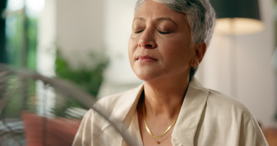 Sweating, woman and fan for heat in home, breathe or symptoms of menopause or hot flash in lounge. House, warm feeling and mature person with hormonal fluctuations, vasomotor and decline of estrogen