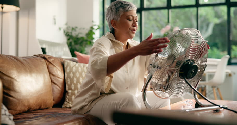 Hot, senior woman and fan on sofa for heatwave, cooling or air circulation in home. Retirement, old person and relax with appliance in living room for summer weather, sweating and refreshing wind