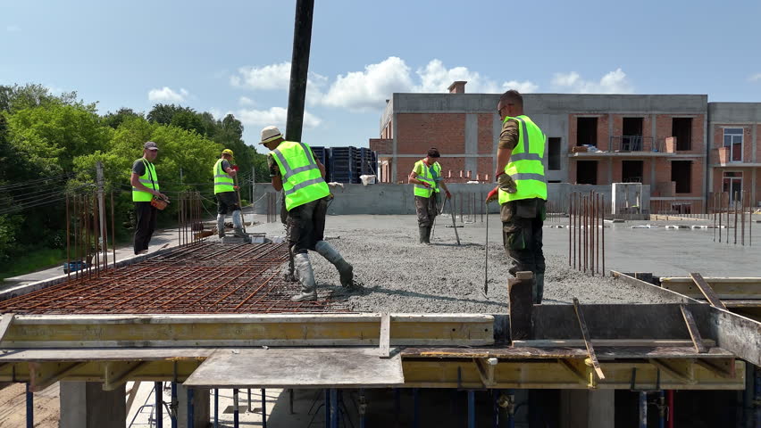 Construction workers pouring concrete on reinforced floor slab, High-rise building site with active teamwork during structural foundation work phase