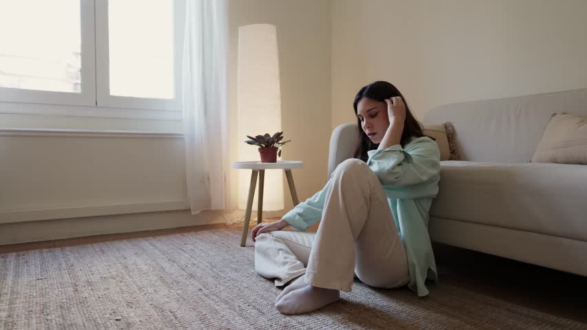 Woman suffering from depression sitting on floor next to sofa