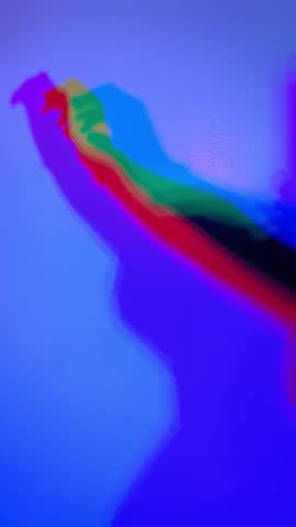 Rainbow shadows of a moving hand and arm being cast on a wall. Red, green, blue, purple, red and yellow shadows move across the blue background in slow motion.