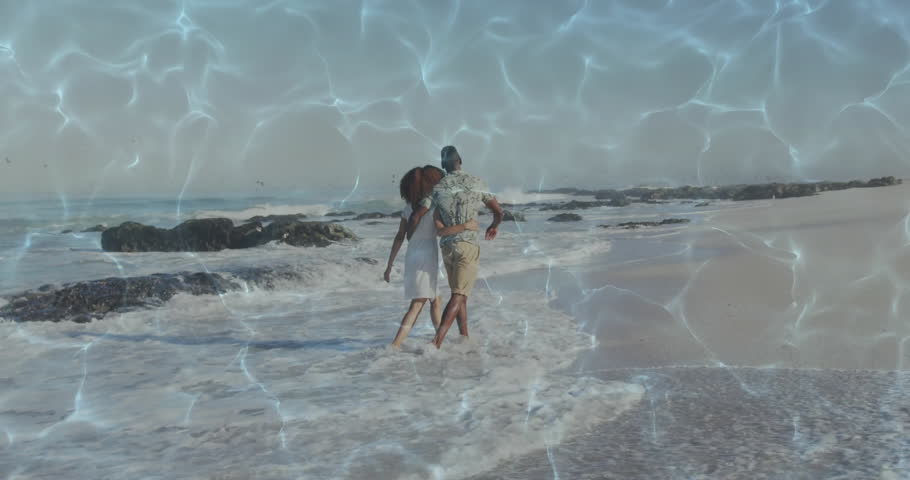 Couple stepping off sand into surf with waves lapping ankles, strolling toward rocky outcrops. Romance, intimacy, seaside, relaxation, harmony, natural, leisure