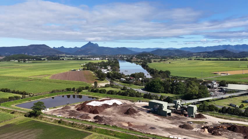 Aerial footage of a sugar mill surrounded by lush green fields and mountains under a clear blue sky