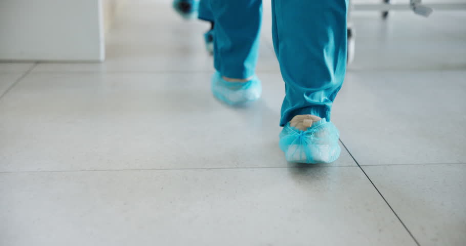 Feet, walking and nurse with bed in hospital corridor with ER operation, treatment or surgery. Moving, medical emergency and healthcare worker pushing patient in hallway to ICU or theater in clinic.
