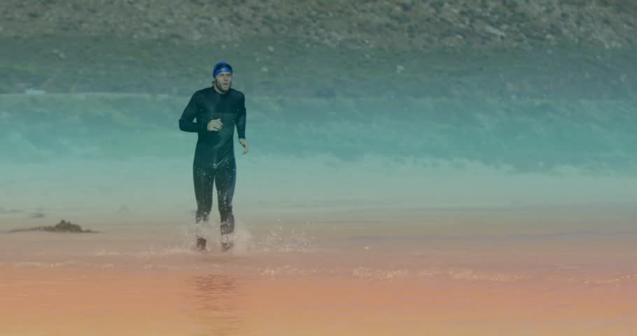 Breaking water surface, man in black wetsuit, blue swim cap running through shallows for triathlon. Athlete, endurance, motion, sport, adventure, aquatic, dynamic