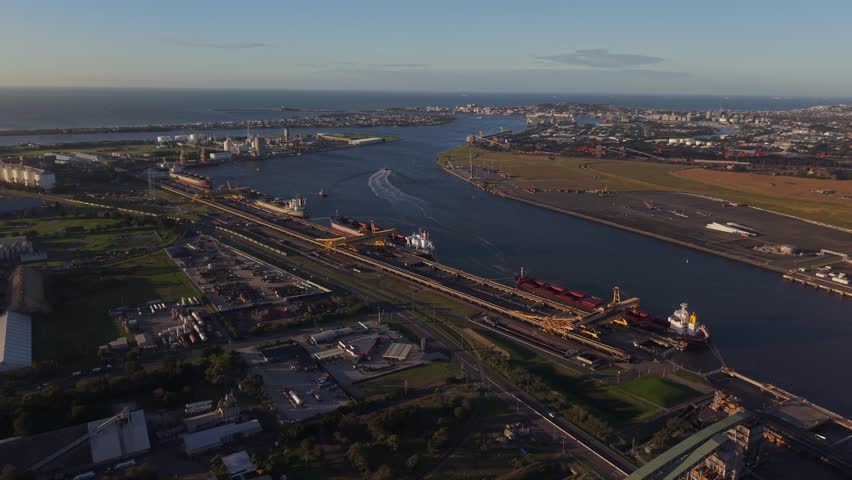 Aerial panoramic establishing of Newcastle shipping port with ocean edge and warehouse structures at sunrise