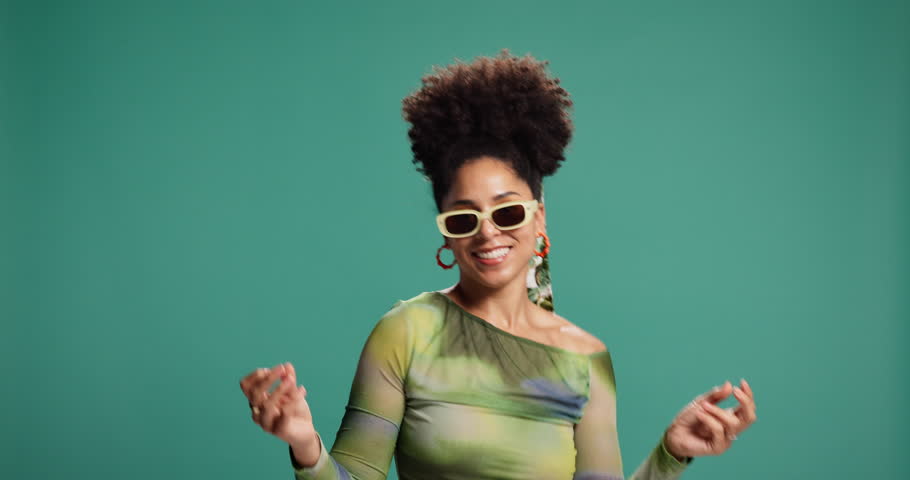 Woman, happy and dancing in studio, sunglasses or confidence with trendy style by background. African person, smile and moving body with rhythm, pride or celebration with edgy fashion with expression