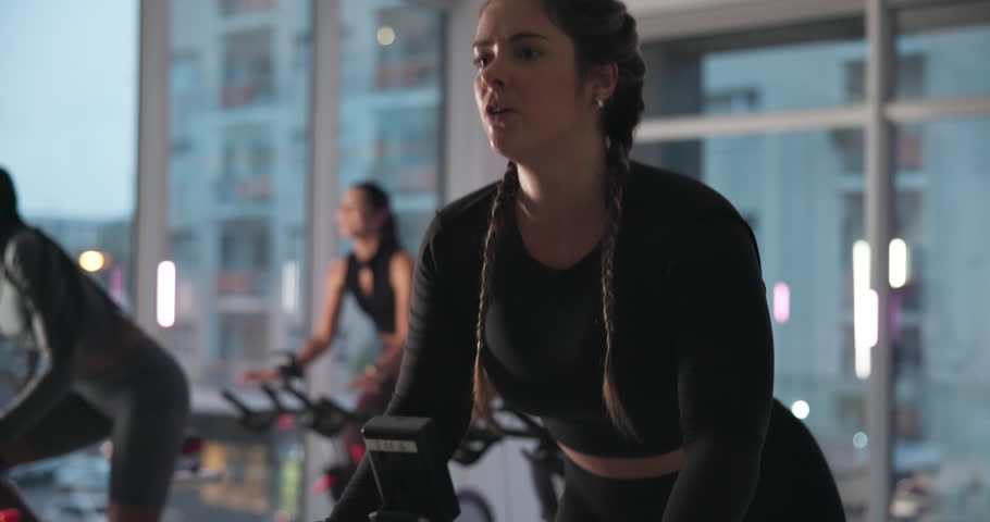 Woman, bike and spin class at gym with smile, strobe lights and coach with motivation for fitness. Person, happy and talk with cycling, workout and training for challenge with group at exercise club