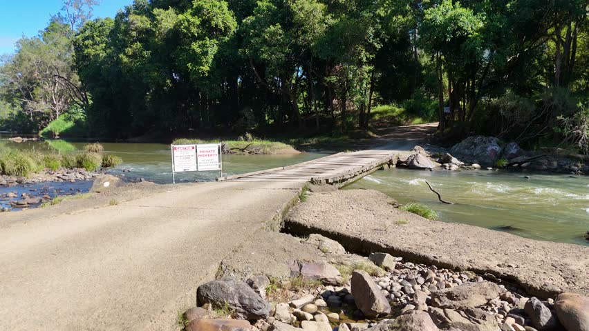 A dirt road crosses a creek with a private property sign. Surrounded by lush greenery under bright daylight