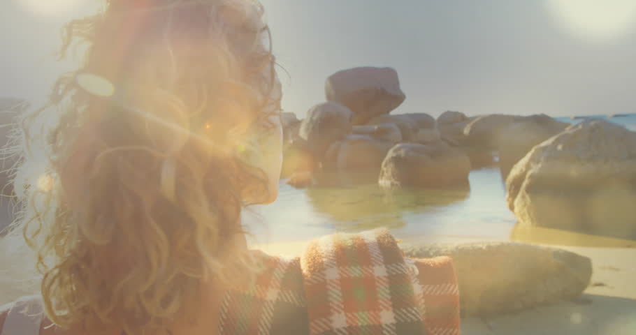 Travel blogger brushing hair and rotating toward shoreline view for travel ad with animated flares. Serenity, adventure, seaside, natural, lifestyle, contemplative, warm lighting