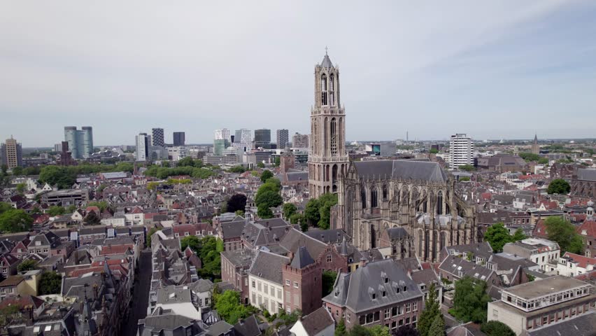Closeup of De Dom church tower in Utrecht within medieval town and high rise modern buildings on horizon behinc. Holland religious tourist destination seen from above.