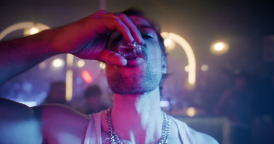 Lively Party Scene with a Stylish Caucasian Man Drinking Alcohol Shots and Kissing a Female While Walking Through a Diverse Male and Female Crowd at an Electronic Music Club Event