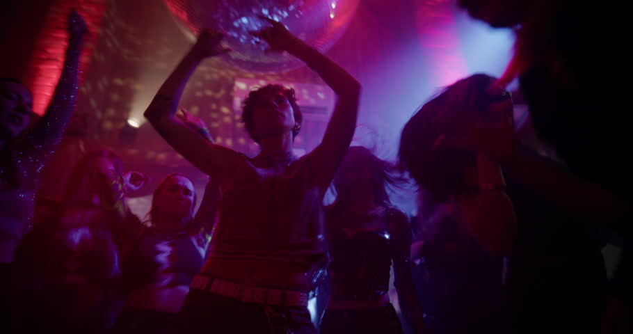Beautiful Female Dancing on a Dancefloor Under Colorful Flashing Lights in a Modern Nightclub. Huge Disco Ball Hanging Above the Excited Party Crowd. Low Angle Dynamic Handheld Footage