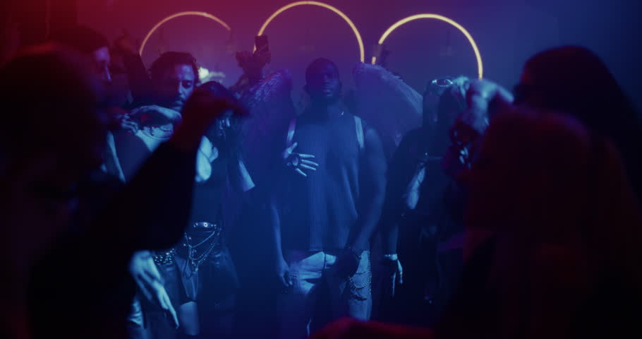 Winged Black Man Joins a Diverse Group of Partygoers on the Dance Floor. African Man Wearing Angel Wings at a Rave Party. Nightclub with Colorful Flashing Lights, Dancing and High-Energy Vibes