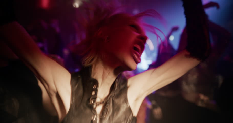 Female Turning Her Head to Look at Camera, Starts Aggressively Dancing with Diverse Crowd to Energetic Electronic Music at a Night Club Party with Colorful Lights and Lively Electrifying Atmosphere
