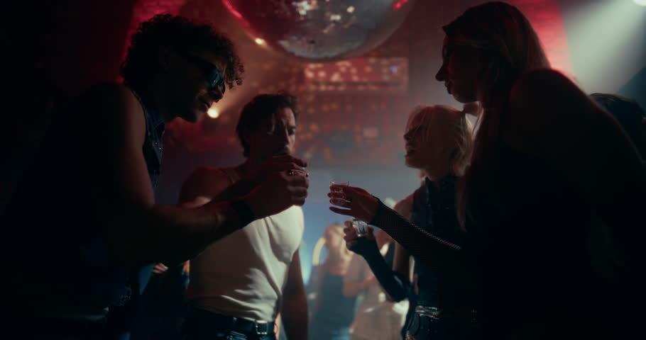 Group of Young Female and Male Friends Gathered at a Nightclub Dance Floor, Taking Shots Together and Celebrating the Night. Diverse People Dance Joyfully Under Flashing Lights