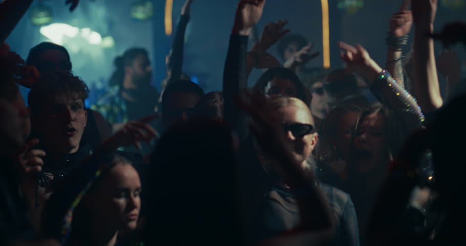 Diverse Party Crowd Enjoying Time in a Nightclub, Dancing Under Dynamic Lights and Pulsating Music. Young Men and Women Having an Emotional Night Out. Footage Focusing on Hands in the Air