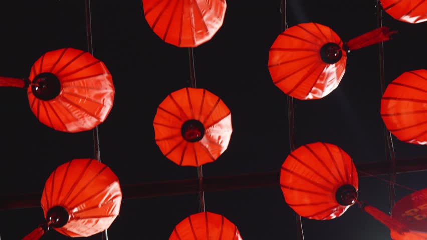 Crimson paper lanterns dangling from overhead wires, softly swinging under starlit sky during festive night celebration of chinese cultural lighting tradition